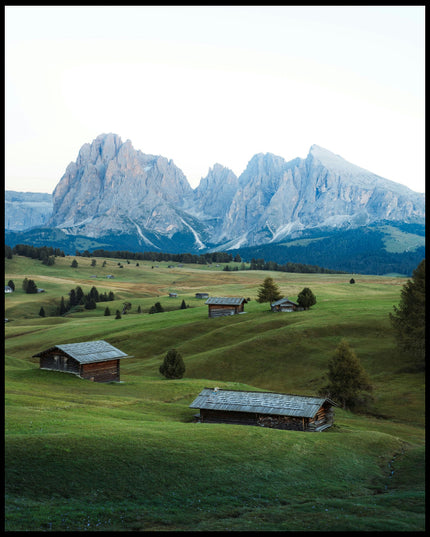 Ein Leinwandbild von einer grünen Alm mit kleinen Hütten und den Dolomiten im Hintergrund.