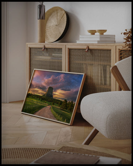 Ein gerahmtes Poster vom Devils Tower bei Sonnenuntergang, an einer Holzkommode angelehnt und stehend auf dem Holzboden