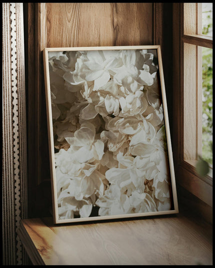 Ein gerahmtes Poster von weißen Blüten in Nahaufnahme, vor einem Fenster an die Wand angelehnt