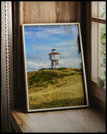 Ein gerahmtes Poster von einem weißen Wasserturm auf der Insel Langeoog, vor einem Fenster an die Wand angelehnt